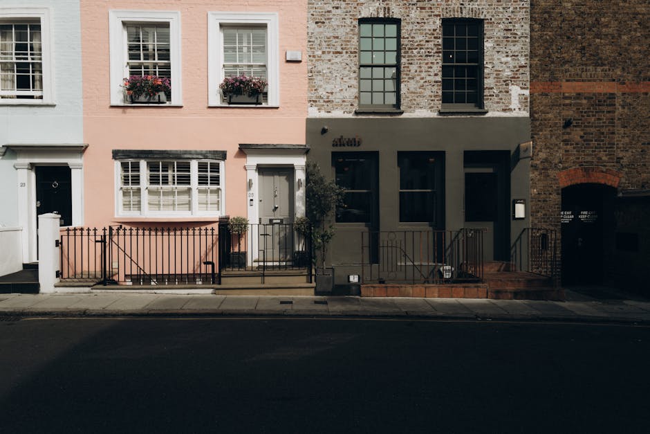 A row of Victorian-style terraced houses in Notting Hill, London, featuring a variety of pastel and bold color facades including pink, teal, and white. The buildings have bay windows with white trims 